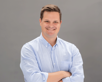 Headshot of Adam Sneed smiling in a light blue button down shirt.