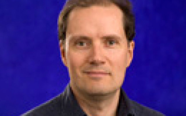 Color photo of Adam Carter in a dark shirt with a blue background.