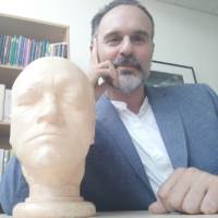 Jason Whittaker sits in a suit jacket with a bust of a head sitting next to him.
