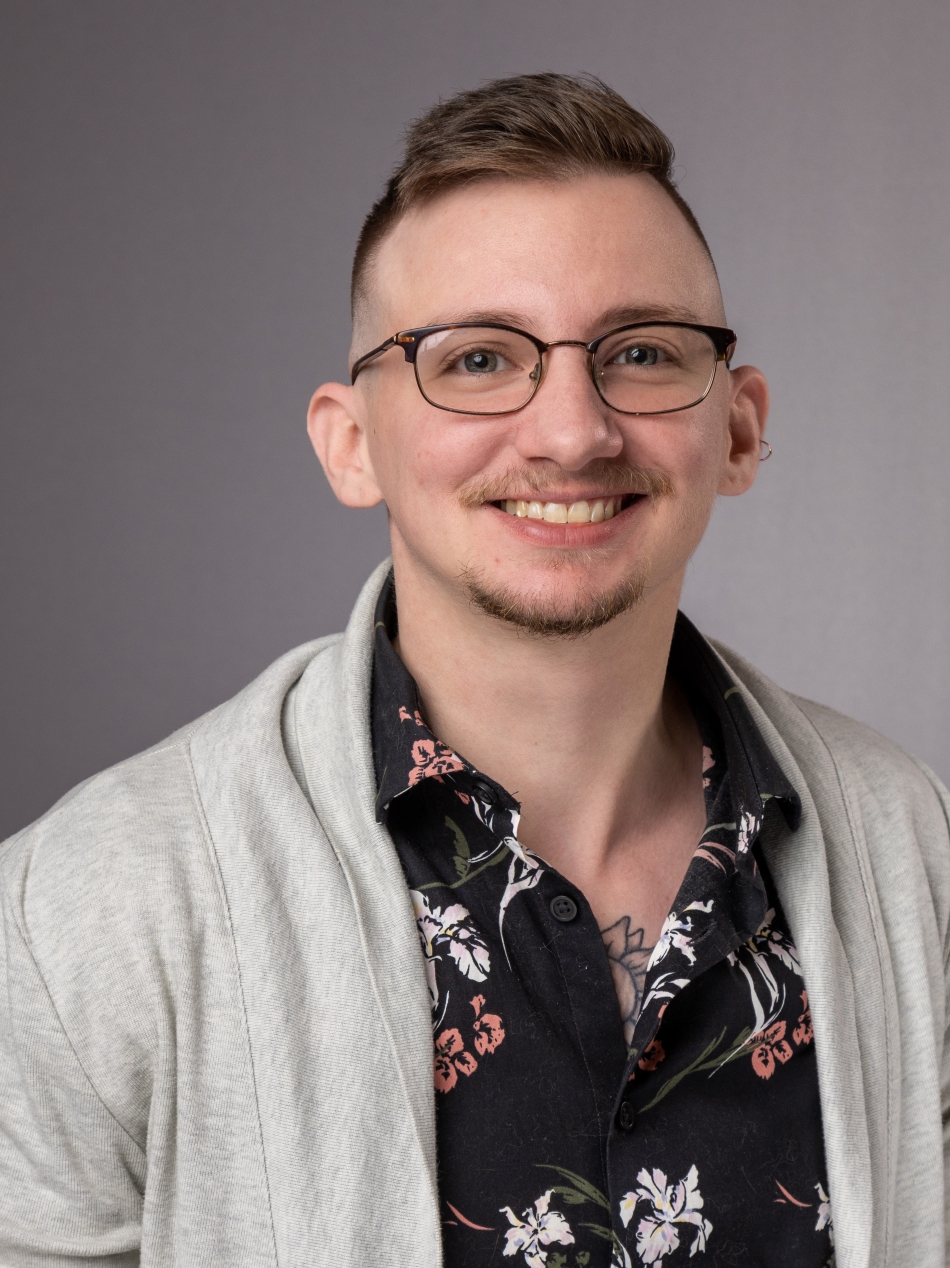 Color headshot of Alex Gatten in a patterned button down and grey cardigan. 